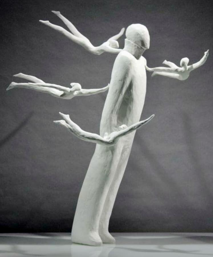 Escultura de hombre con cuatro figuras humanas volando alrededor